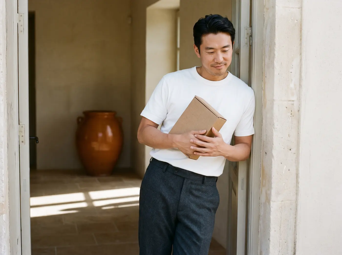 A man at his front door holding a plain, unmarked cardboard box